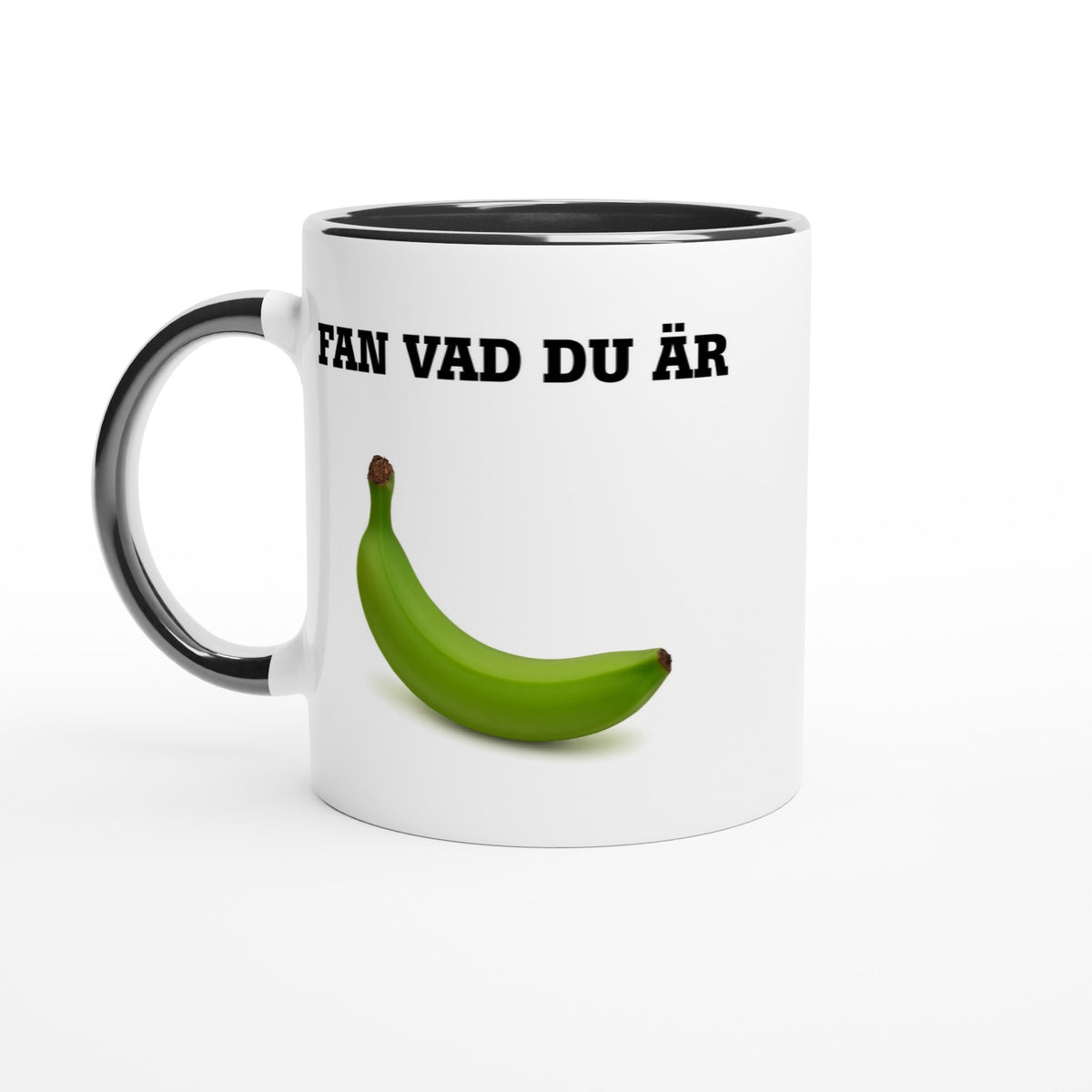 Vit mugg med svart handtag och svart insida med texten Fan vad du är och en grön omogen banan